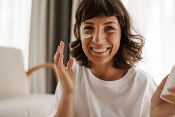 Femme de 40 ans qui sourit en s'appliquant une crème sur le visage